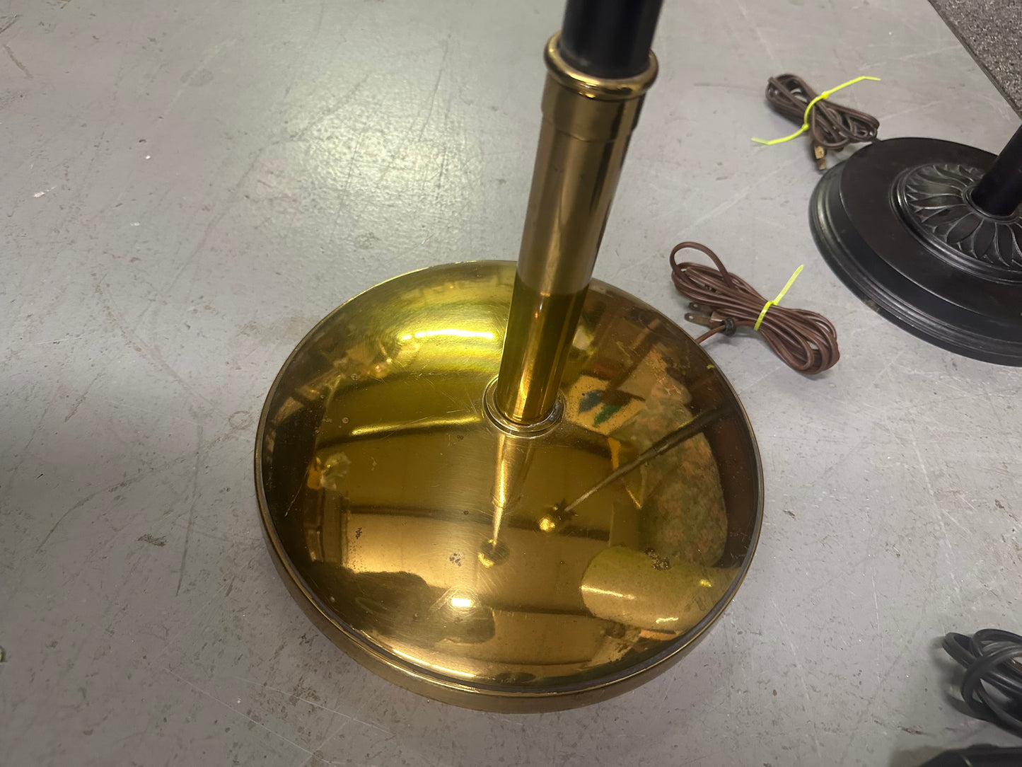 Brass lampshade on a stand with a cord on a gray floor.