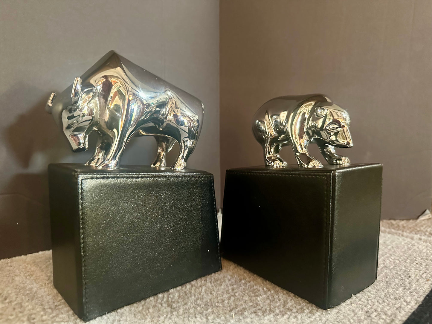Two metallic animal figurines on black stands against a neutral background