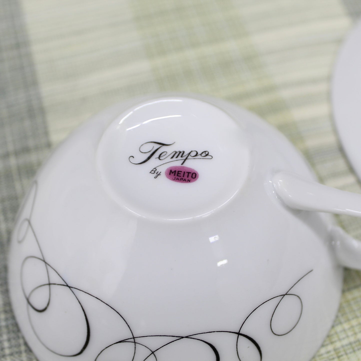 Close-up of the bottom backstamp on a vintage porcelain cup showing a pinkish mauve magenta circle reading Meito Japan with the pattern name Tempo written in black cursive script above it.