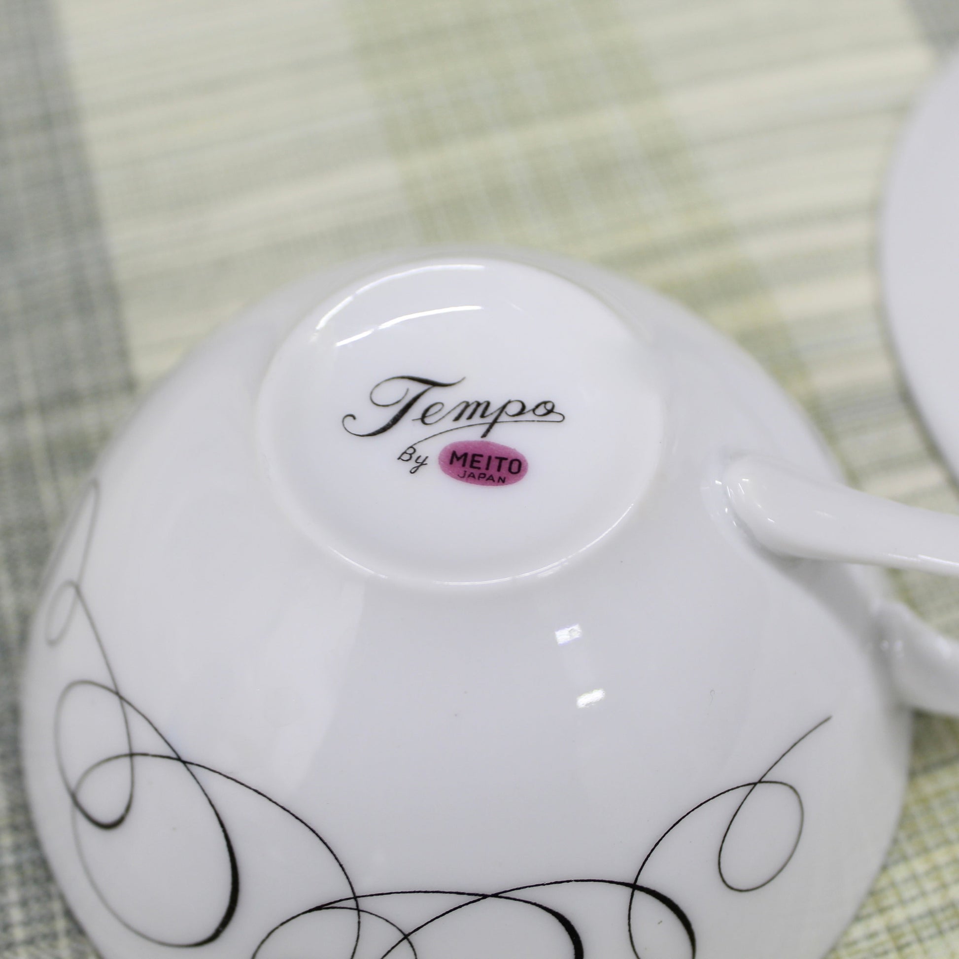 Close-up of the bottom backstamp on a vintage porcelain cup showing a pinkish mauve magenta circle reading Meito Japan with the pattern name Tempo written in black cursive script above it.