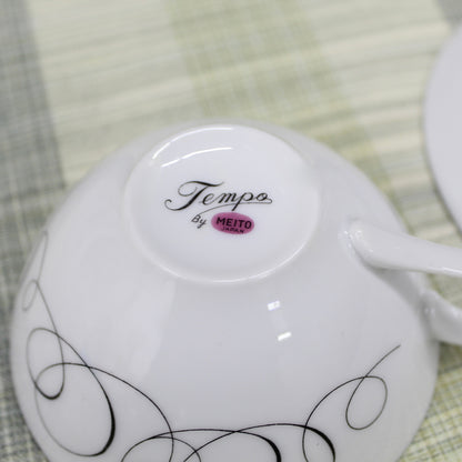 Close-up of the bottom backstamp on a vintage porcelain cup showing a pinkish mauve magenta circle reading Meito Japan with the pattern name Tempo written in black cursive script above it.