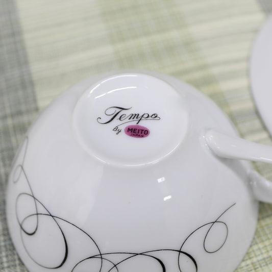 Close-up of the bottom backstamp on a vintage porcelain cup showing a pinkish mauve magenta circle reading Meito Japan with the pattern name Tempo written in black cursive script above it.