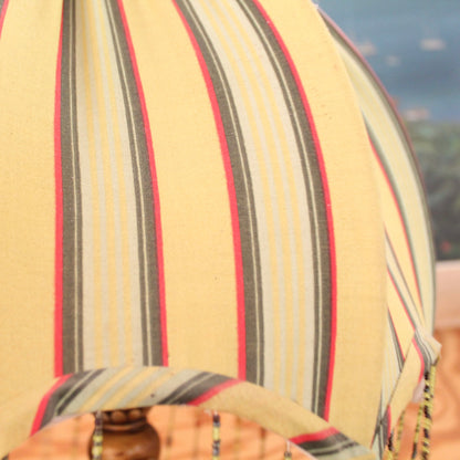 Dome-shaped fabric lamp shade with vertical stripes in beige, gray, yellow, and red.