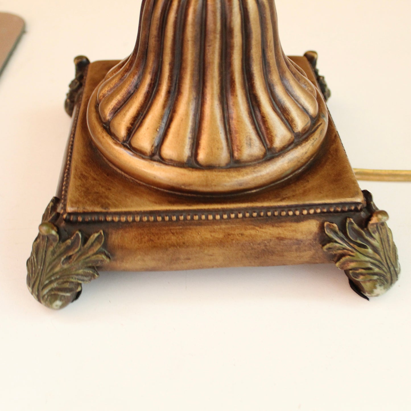 Close-up of an ornate vintage-style lamp base in a distressed bronze finish, with a fluted central column, decorative corner feet. 