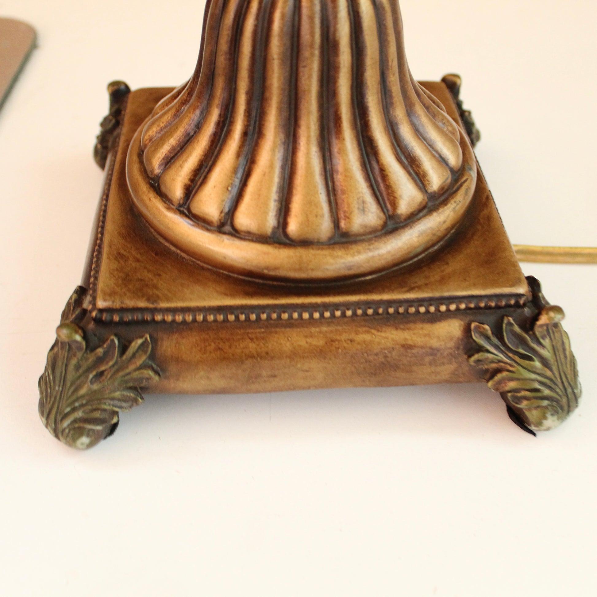Close-up of an ornate vintage-style lamp base in a distressed bronze finish, with a fluted central column, decorative corner feet. 