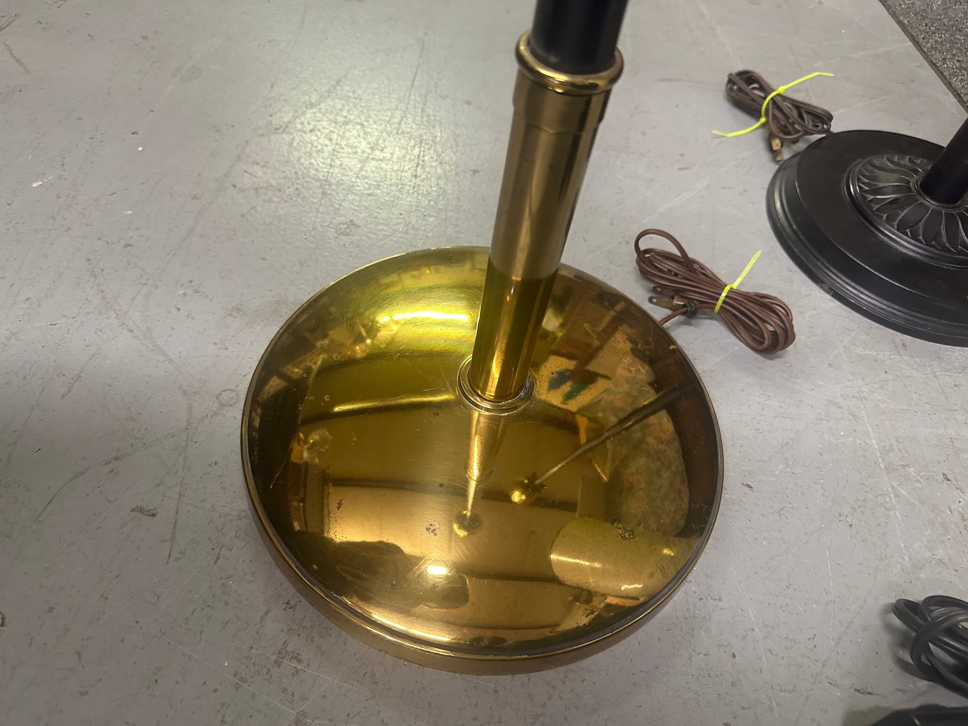 Brass lampshade on a stand with a cord on a gray floor.