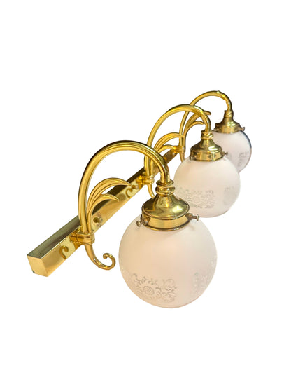 Wall-mounted light fixture with gold frame and white glass shades on a dark background