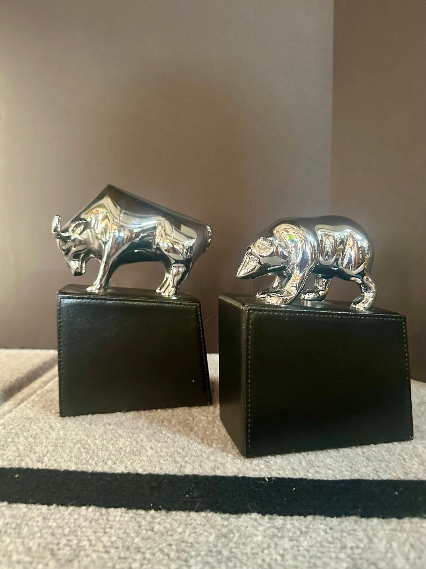 Two metallic bull and bear figurines on black bases against a neutral background