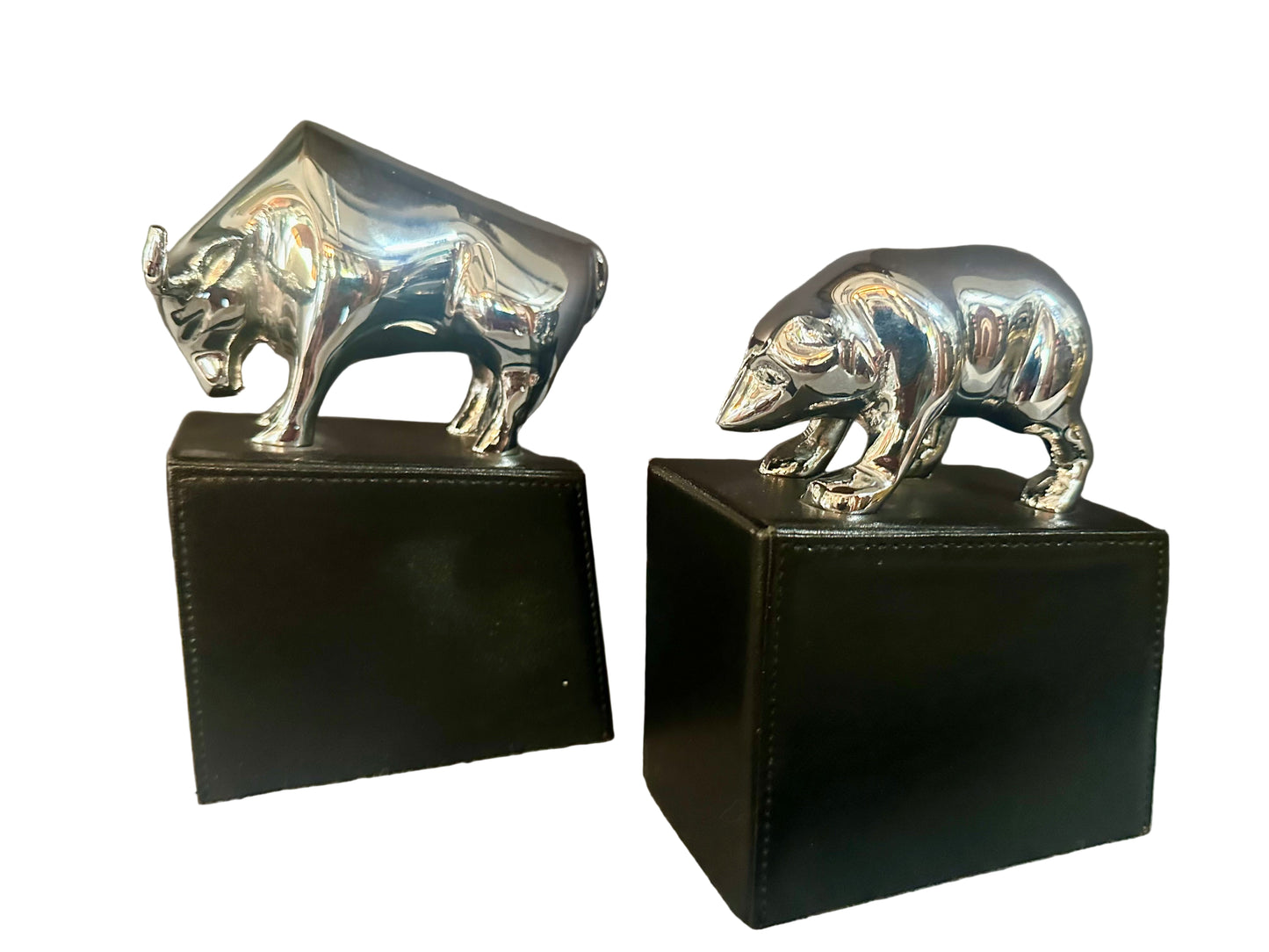 Silver bull and bear figurines on black stands against a neutral background