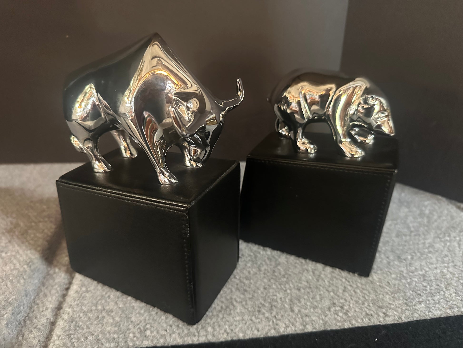 Two metallic bull figurines on black stands against a dark background