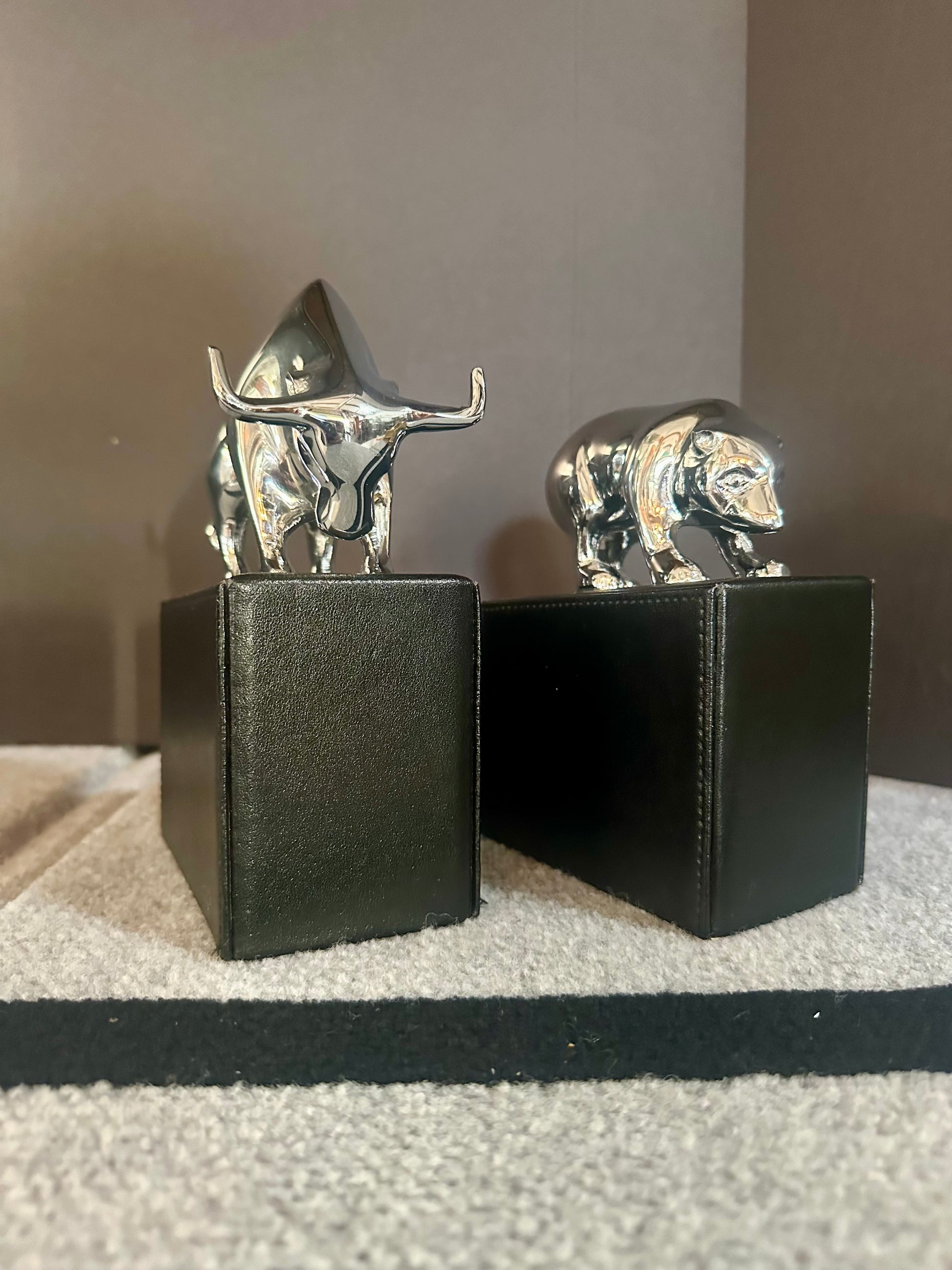 Two metallic animal figurines on black stands against a neutral background