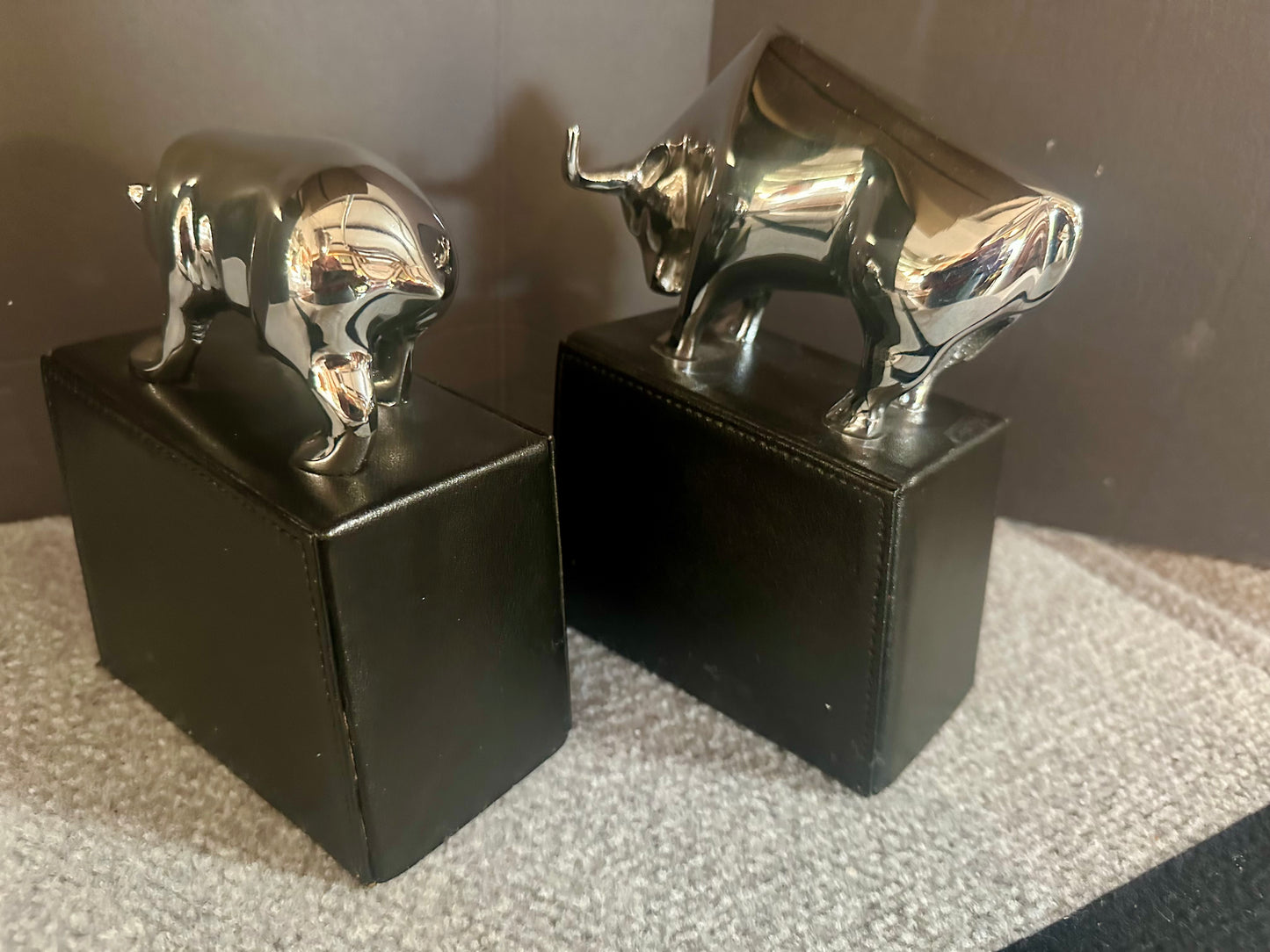 Two metallic bull figurines on black bases against a neutral background