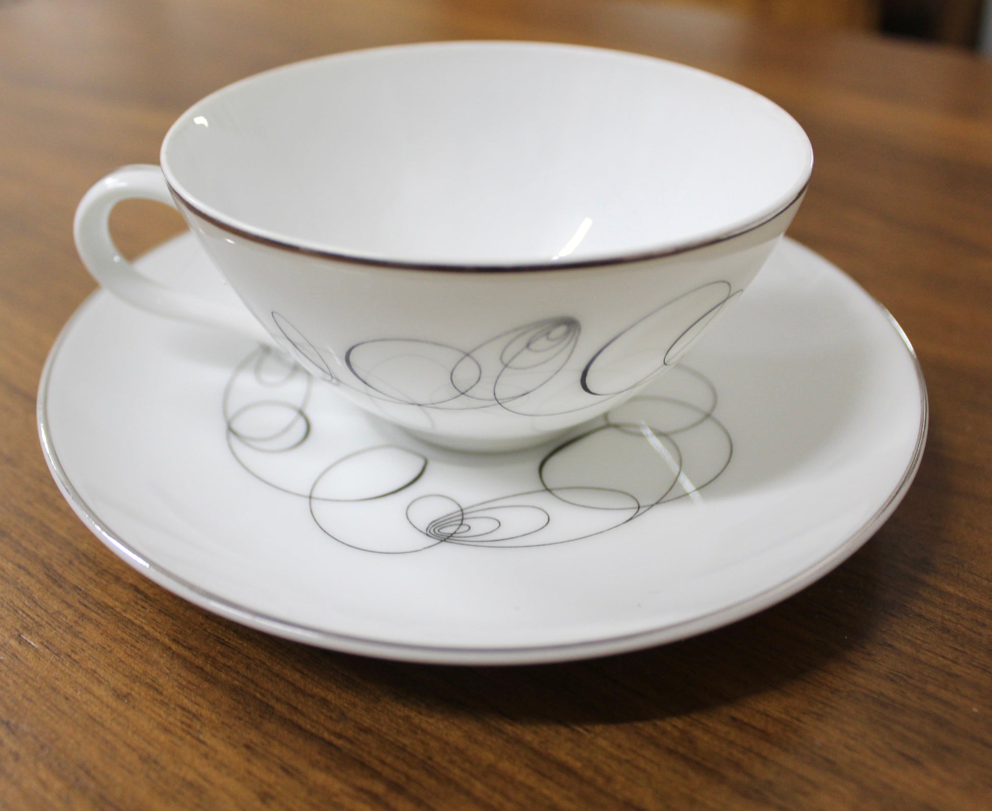 Side view of a vintage Meito China Tempo pattern flat cup showing the mid-century modern black atomic spiral design and reflective platinum rim.