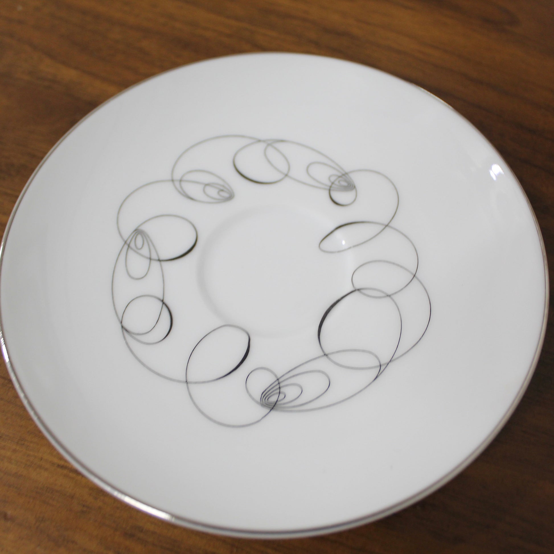 top down view of a vintage Meito China Tempo pattern saucer showing the mid-century modern black atomic spiral design and reflective platinum rim.