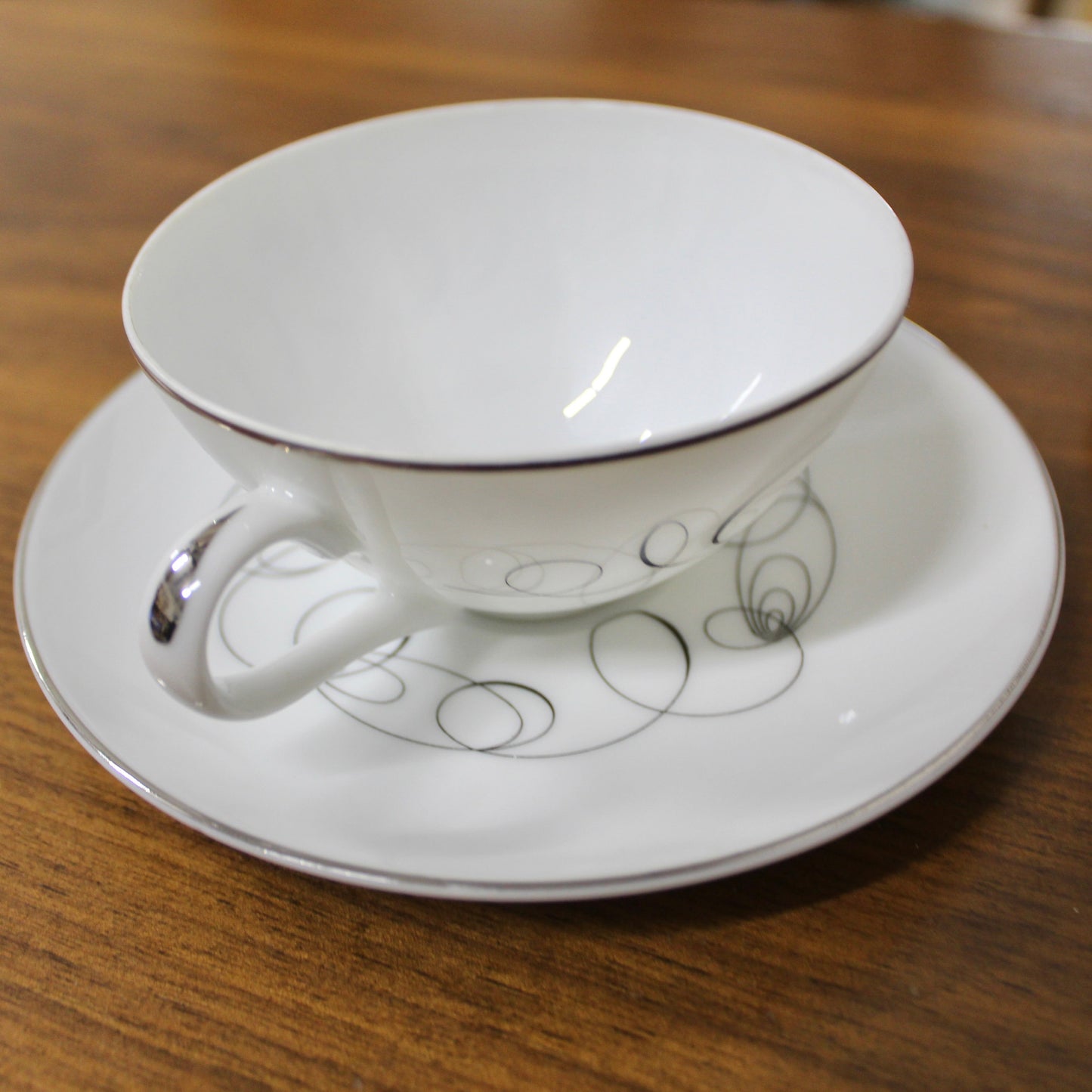Side view of a vintage Meito China Tempo pattern flat cup showing the mid-century modern black atomic spiral design and reflective platinum rim.